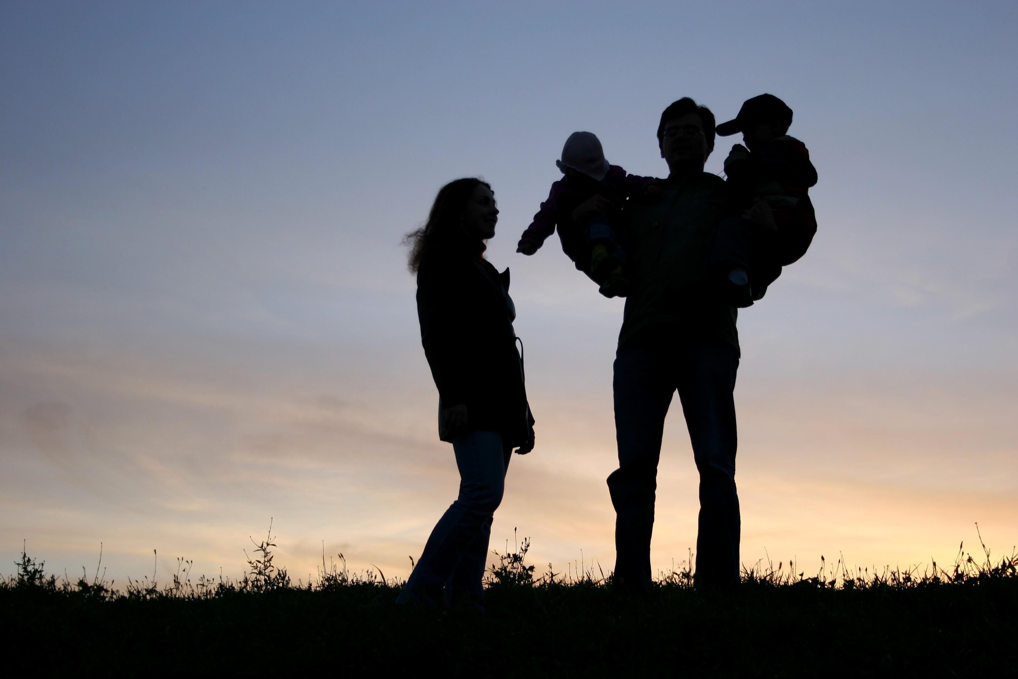 family with children on hands, sunset sky